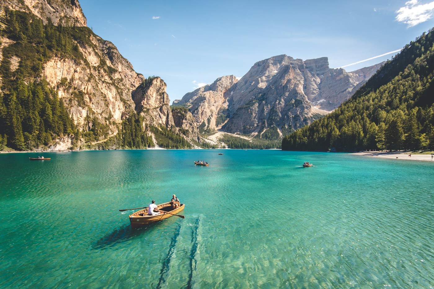 A turquoise lake beneath forested mountains, with small boats on the still water